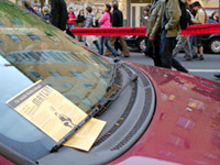 Mayday-Flyer unter dem Scheibenwischer eines Autos, im Hintergrund Demonstrierende